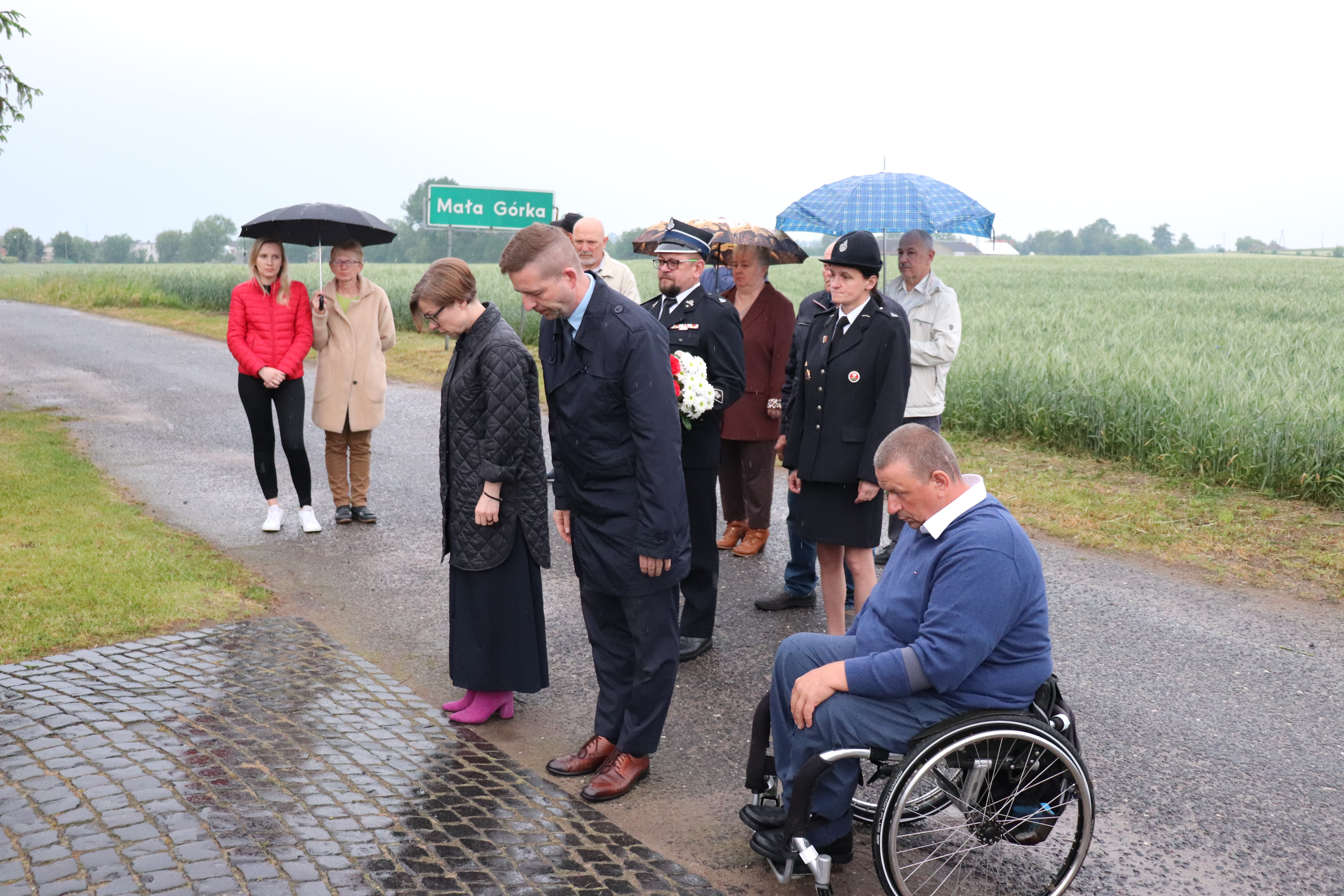 Trzy osoby kłaniają się pod pomnikiem. Od lewej Pani Wiceburmistrz, Pan Burmistrz oraz Przewodniczący Rady Miejskiej poruszający się na wózku. 